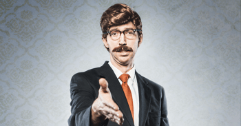 A stereotypical corporate manager type business man in full suit, big combover hairstyle and mustache looks at the camera with arm extended for a handshake. Intentional cliche look for humor.